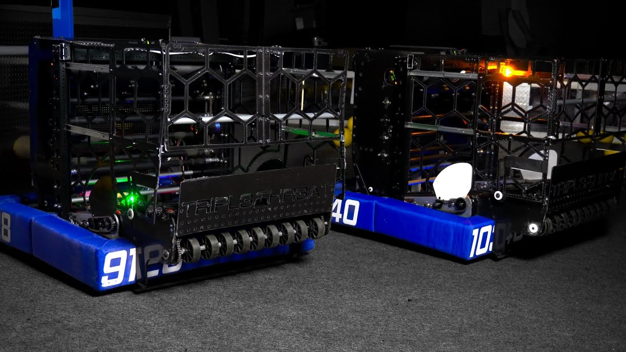 The 9128 and 10340 robots side by side at the 2026 reveal, both with blue bumpers, the near one lettered TRIPL3 THR3AT above its intake rollers.